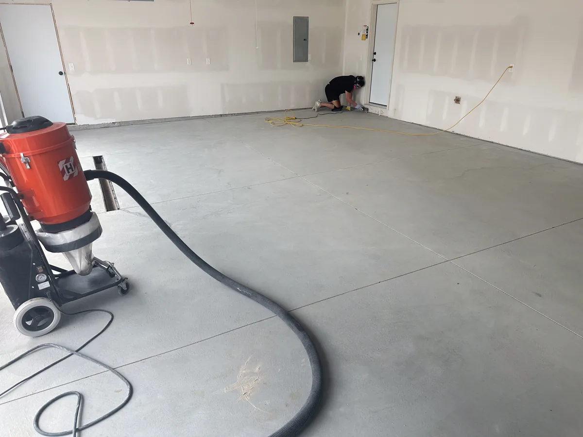 Crew edge grinding a garage slab with a dust extractor running