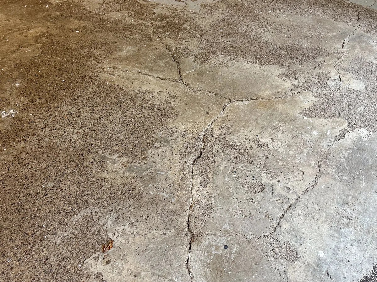 Cracked and stained concrete slab with bits of an old coating