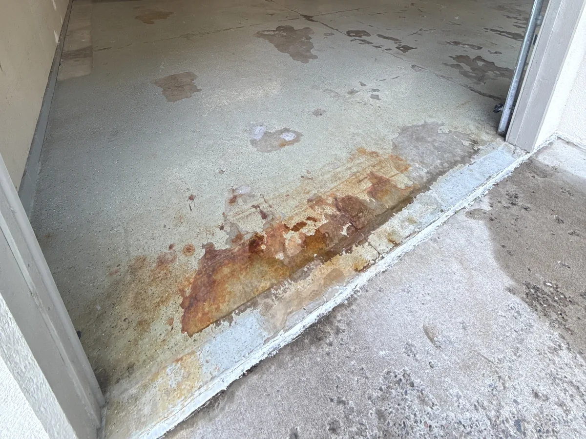 Rust stains and wear on a concrete garage slab near the door