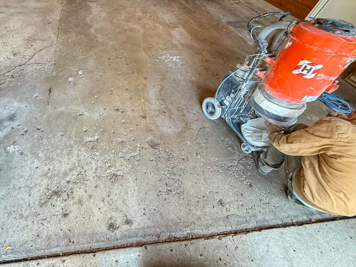 Crew edge grinding a pitted garage slab next to wood paneled walls