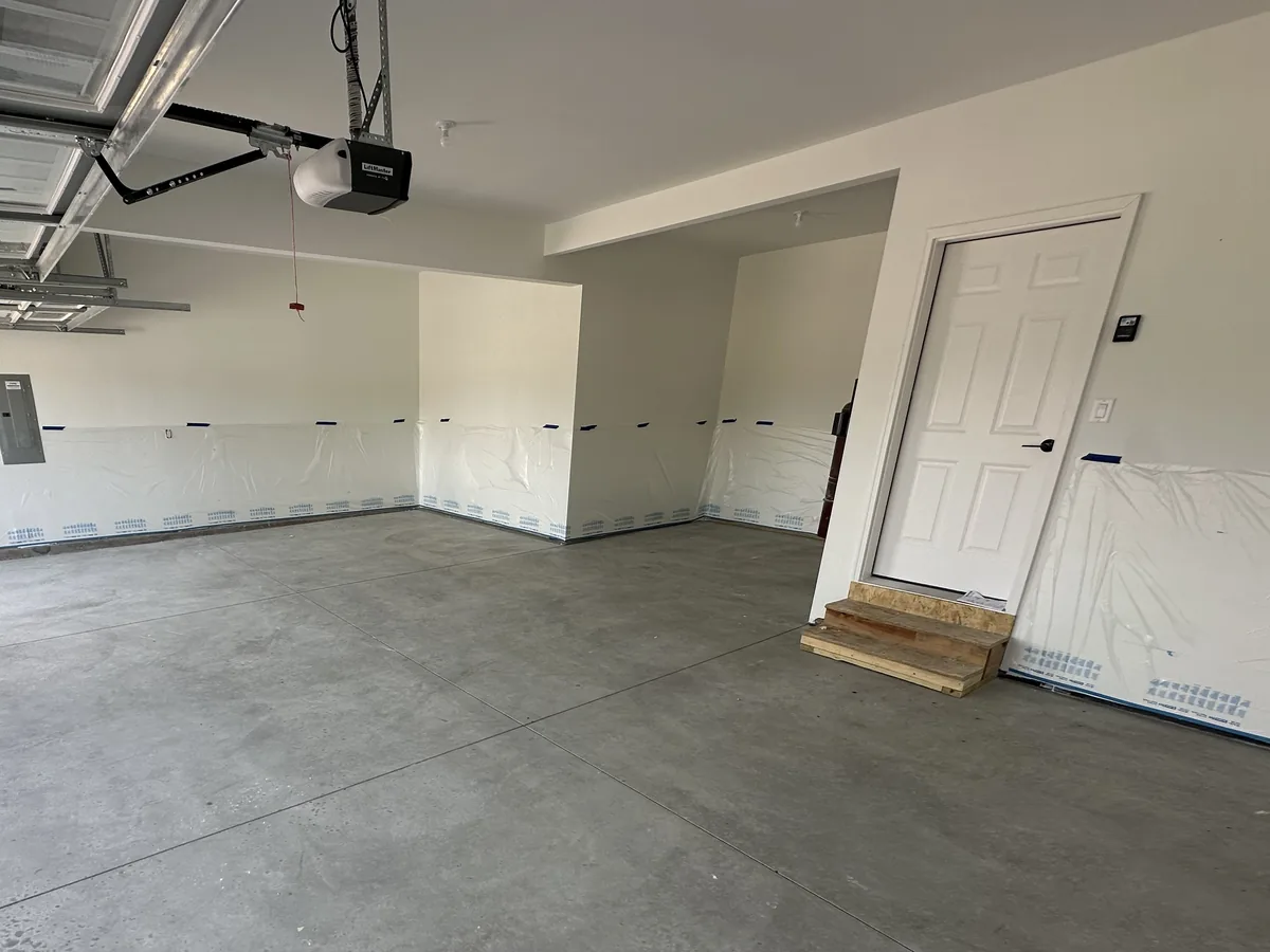 Bare concrete floor in a newer garage with plastic taped over the lower walls