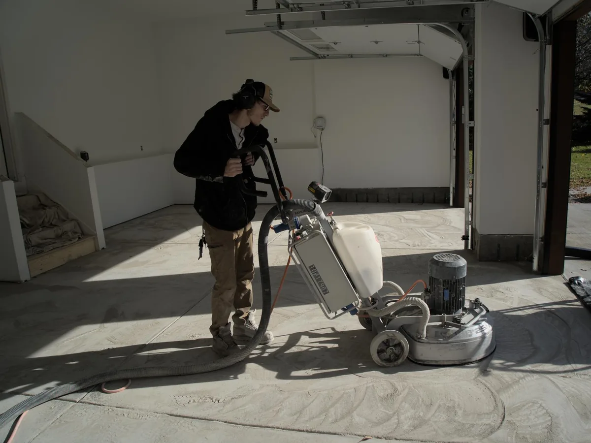 Crew member running a diamond grinder on a bare garage slab