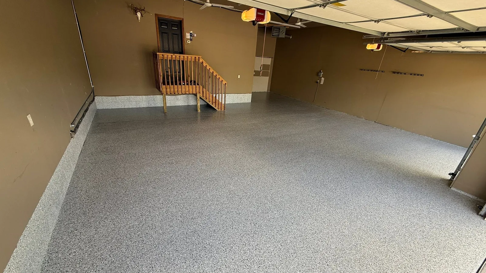 Gray flake garage floor coating in a garage with brown walls and a wood stair railing