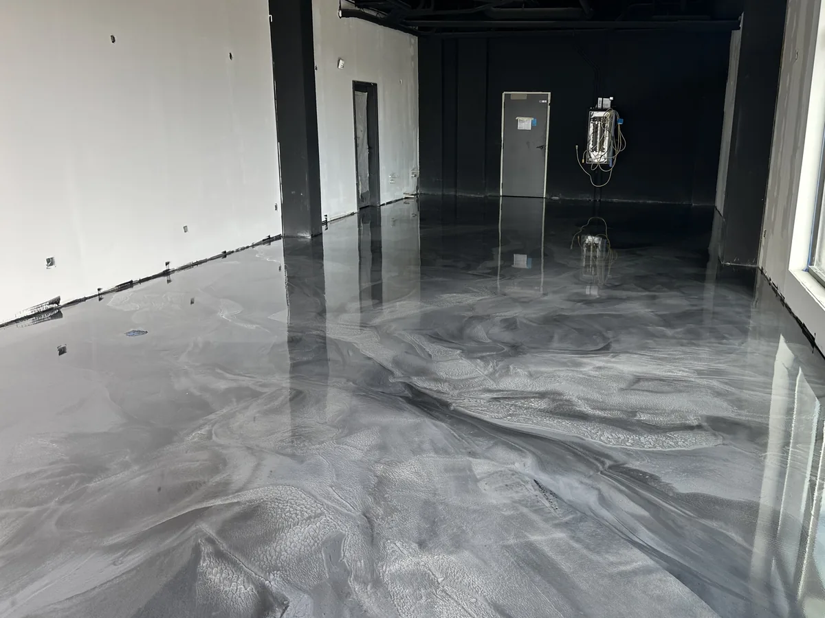 Silver and gray metallic epoxy floor in an empty commercial space with a black ceiling