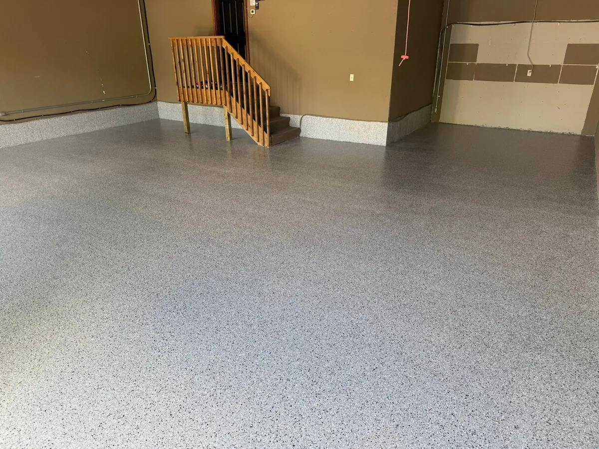 Finished gray flake garage floor with brown walls and a wood stair railing